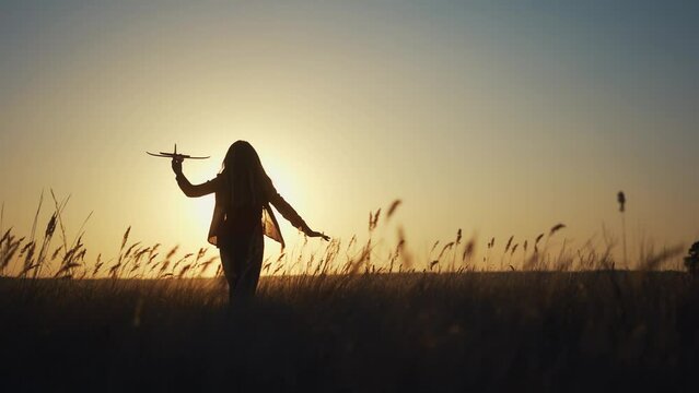 girl runs across the field. concept of a happy childhood and loving family. girl runs across a field with an airplane in her hands, silhouette of a child, lifestyle sunset on the background