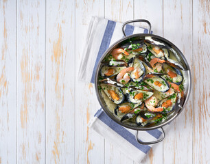 Mussels clams in cream sauce in a pan on a wooden table copy space for text.