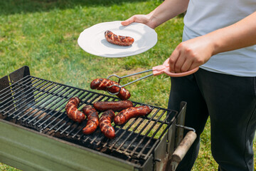 Grilled pork sausage on a cast iron grill. Hand of young woman grilling some meat. Young female...