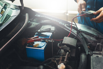 Auto mechanic uses multimeter to check the voltage level in a car battery during a vehicle maintenance procedure..