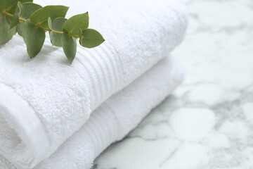 Fototapeta na wymiar Folded terry towels and eucalyptus branch on white marble table, closeup