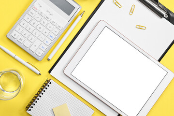 Modern tablet, stationery and glass of water on yellow background, flat lay. Space for text