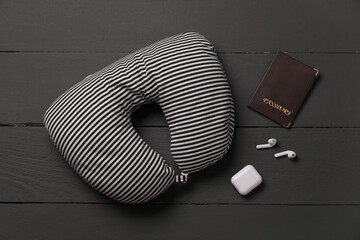 Striped travel pillow, passport and earphones on black wooden background, flat lay