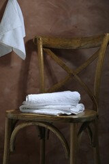 White terry towels on wooden chair against brown background