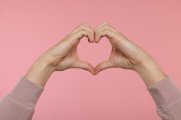 Man showing heart gesture with hands on pink background, closeup