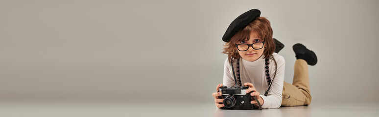 boy photographer in beret and glasses taking photo on camera and lying on floor, banner