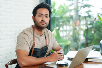 Close-up of face of handsome bearded Indian man working with laptop. Businessman. Coffee shop. Small family business. Sitting and working is stressful. Think a lot about store's income and expenses.