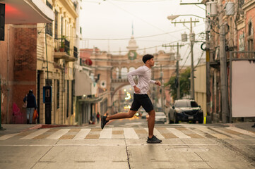 Portrait of a young man running through the streets of downtown while exercising. A healthy...