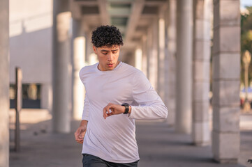 A young man with a smartwatch on his hand to count calories does exercises outdoors. Healthy...