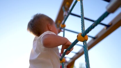 child plays on the playground. concept of a happy childhood and loving family. a child smiles joyfully and climbs a ladder on a lifestyle playground, the glare of the sun in the background