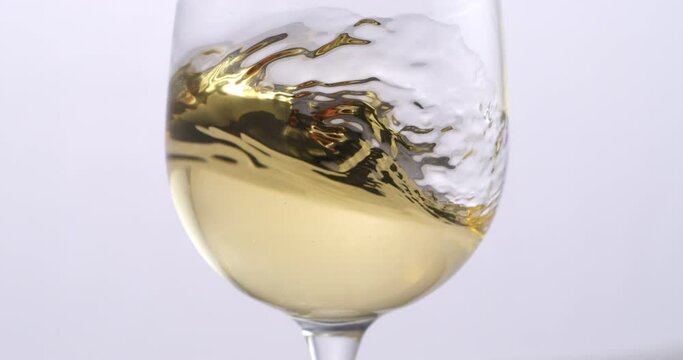 Super slow motion close up of white wine is being swirled in transparent glass by winemaker or sommelier for flavor tasting and quality checking isolated on light background at 1000 fps.