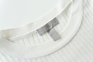 Close-up of a white knitted sweater neckline with a grey tag, highlighting fabric texture and...