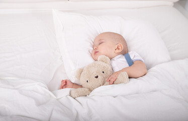 Portrait of adorable cute baby boy lying on white bed with teddy bear in hands sleeping toddler with place for text toddler dream