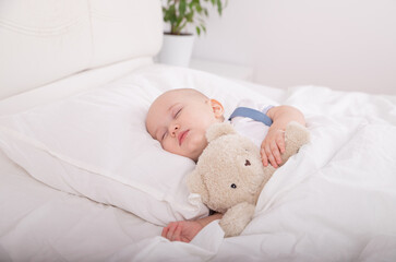 Portrait of a little child boy lying on a pillow in white color White bed white bed on green flower background hugging Teddy Bear for Sleep, Sleep Toys