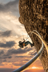 Person climbing, rappelling on mountain at sunset with golden light, sky with clouds, oranges