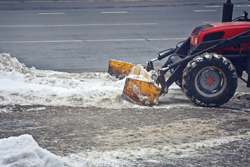 Tractor removes snow from sidewalk. Cleaning and clearing snowy road. Snow removal work after...