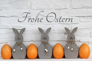 Fröhliche Osterhasen mit Ostereiern vor einer Wand mit der Beschriftung Frohe Ostern.