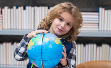 School kid pupil looking at globe in library at the elementary school. World globe. School kid 7-8 years old with book go back to school. Little student. Education concept.