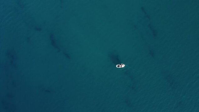 drone, vista dall'alto. Pescatore su piccola barca in mare limpido e azzurro raccoglie rete da Pesca. 
