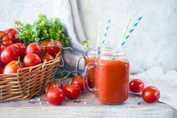 Freshly squeezed tomato juice in a glass cup and ripe tomatoes in a basket, on a wooden table