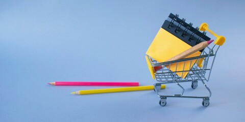 Miniature shopping cart with school supplies on blue background. Back to school concept.