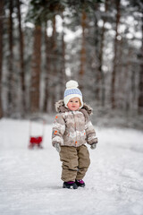 Fototapeta na wymiar Little baby child in a warm jumpsuit walks in a snowy winter forest