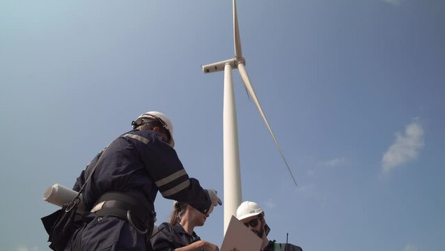 Engineers man and woman inspecting construction of WIND TURBINE FARM. WIND TURBINE with an energy storage system operated by Super Energy Corporation. Workers Meeting to check AROUND THE AREA.