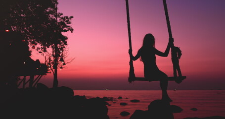 Woman silhouette sway on wooden rope swing against bright pink sunset. Vacation on beautiful seacoast. Travel, tourism, holiday on paradise Thailand Island. Nature landscape in sunrise.
