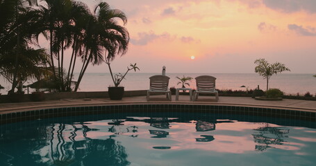 Girl silhouette near swimming pool at sunset time. Colorful sunrise sky reflected in calm water. Relax, retreat, meditation. Travel, tourism, holiday spa vacation.