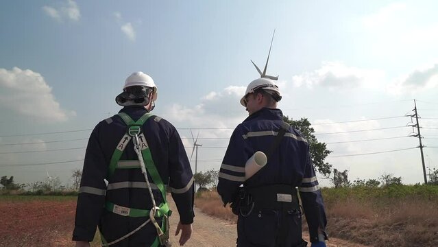 Engineers man and woman inspecting and walking of WIND TURBINE FARM. WIND TURBINE with an energy storage system operated by Super Energy Corporation. Workers Meeting to check AROUND THE AREA.