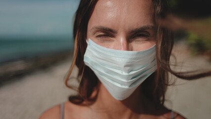Woman walking summer beach wearing medical mask. Young female in bikini enjoy outdoor lifestyle...