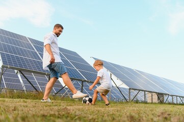 A father and his little son play football near the solar panels. The concept of renewable energy.