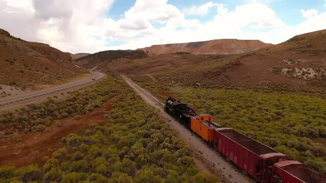 Aerial: Drone Forward Shot Of Railway And Vehicles Moving In Semi Arid Desert Under Cloudy Sky - Ely, Nevada