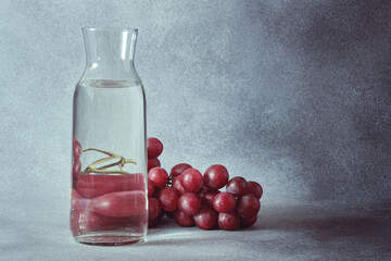 Elegant Water Carafe with Red Grapes on Textured Grey Background