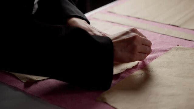 Tailor's Hand Arranging Sewing Patterns on Textile. A tailor's hand placing sewing patterns on a pink fabric surface.