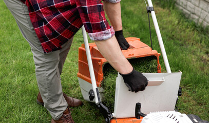 Gardener man in casual clothes carries plastic lawn mower box with cut grass of modern gasoline...