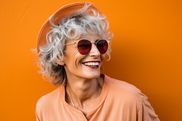 Portrait of a happy senior woman with sunglasses over orange background.