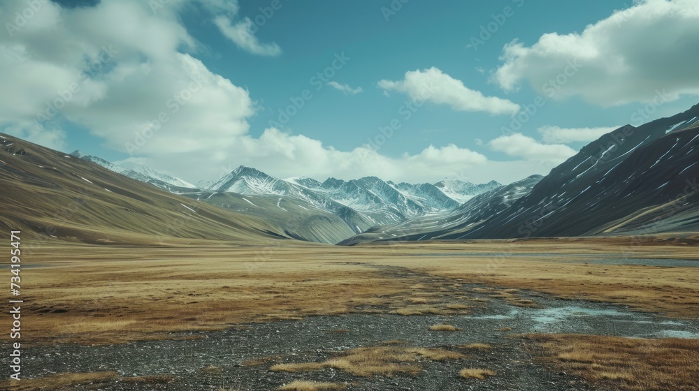 Poster a wide open field with a stream running through it and a mountain range in the distance with snow on