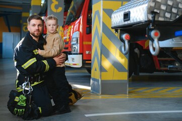 A firefighter take a little child boy to save him. Fire engine car on background