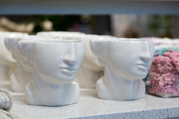 Unique ceramic face-shaped pots or vases on a shelf, with a glossy finish and subtle details,...