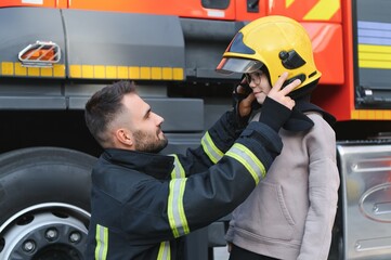 Fototapeta premium A firefighter take a little child boy to save him. Fire engine car on background