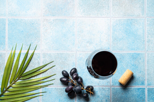 Red wine on blue background. Glass wine with grape and palm leaves. Flat lay image with copy space.