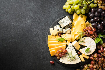 Fototapeta na wymiar Cheese platter with craft cheese assortment and grape at black background. Top view with copy space.