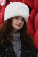 portrait of beautiful young woman in white fur winter hat and dark winter coat outside in winter