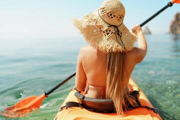 Woman in kayak back view. Happy woman with long hair in a swimsuit and hat floating in kayak on the...
