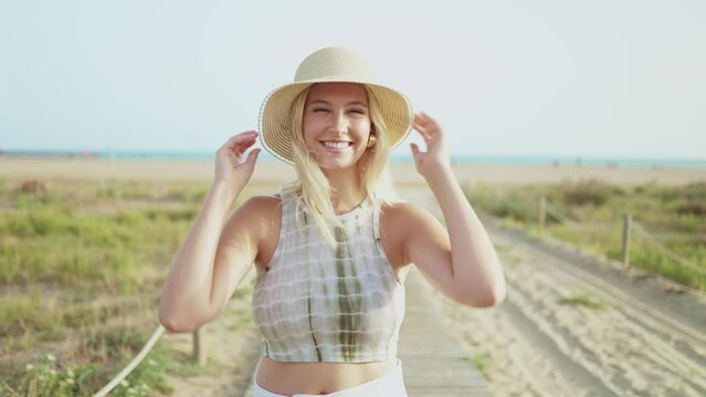Beautiful young woman with a hat smiling at the camera enjoying her holiday on a sunny summer day at the beach. Concept of summer holidays, weekend and happiness. Joyful or holiday adventure or travel