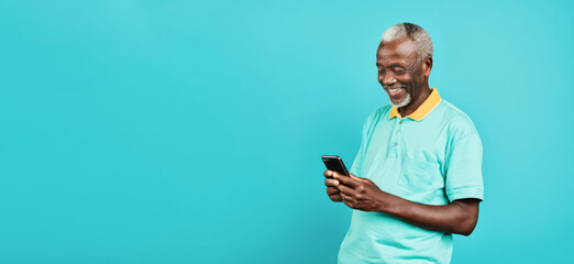 Portrait of smiling happy African senior man with gray hair looking at mobile phone on light blue cyan background, studio shot, copy space for text