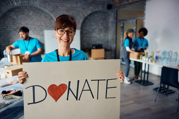 Happy volunteer holding placard with 'donate' message at community center and looking at camera.