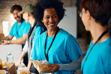 Happy black volunteer talking to her coworker while working at food bank.