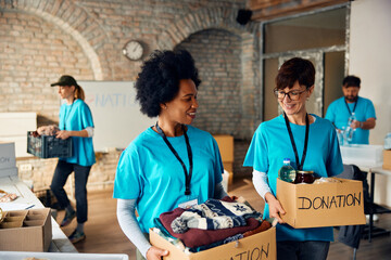 Happy multiracial charity workers carrying cardboard boxes with donated food and clothes at...